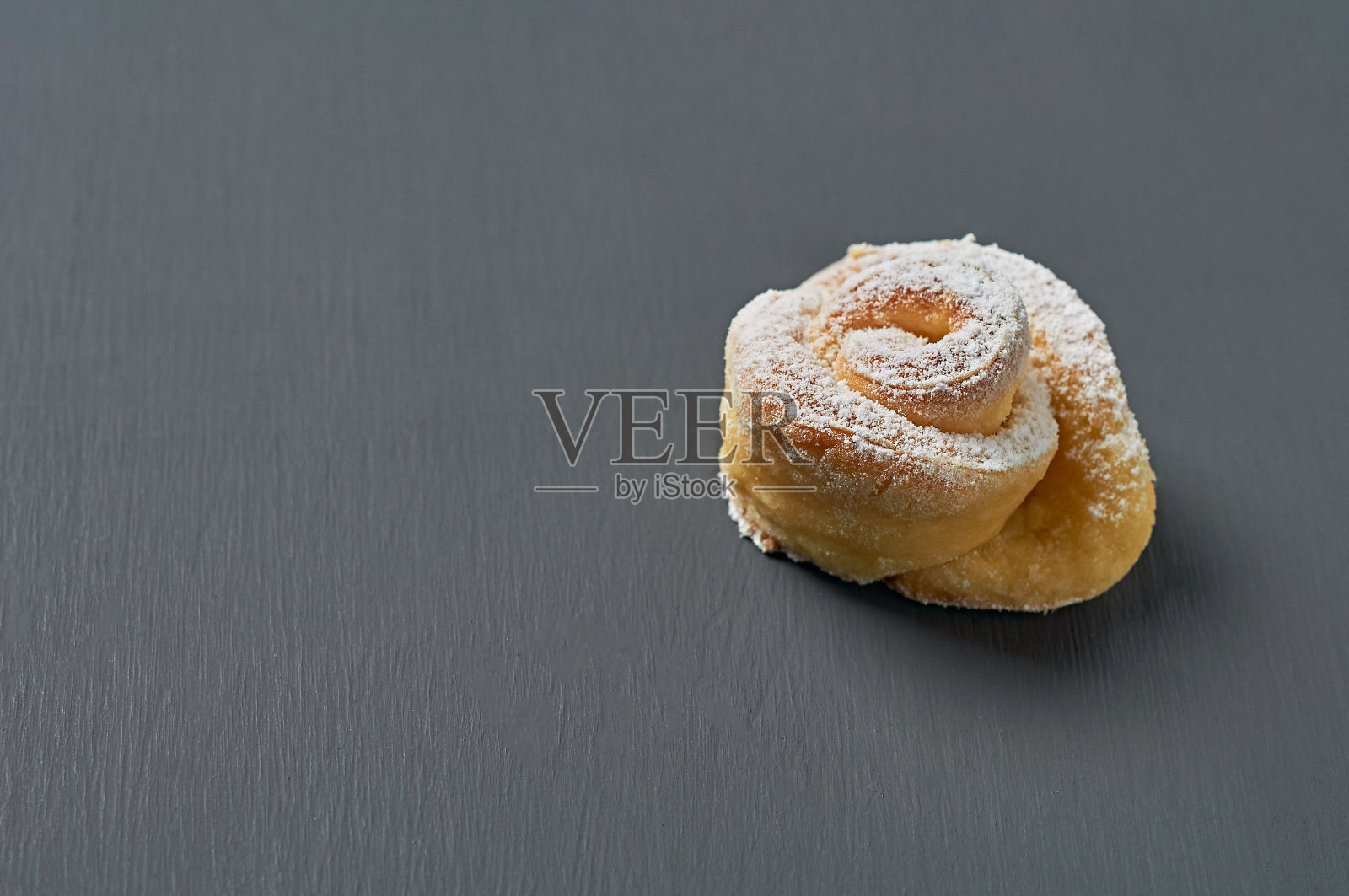 黑色的混凝土桌子上放着一个自制的玫瑰糖粉面包。职场糖果。空间的文本照片摄影图片