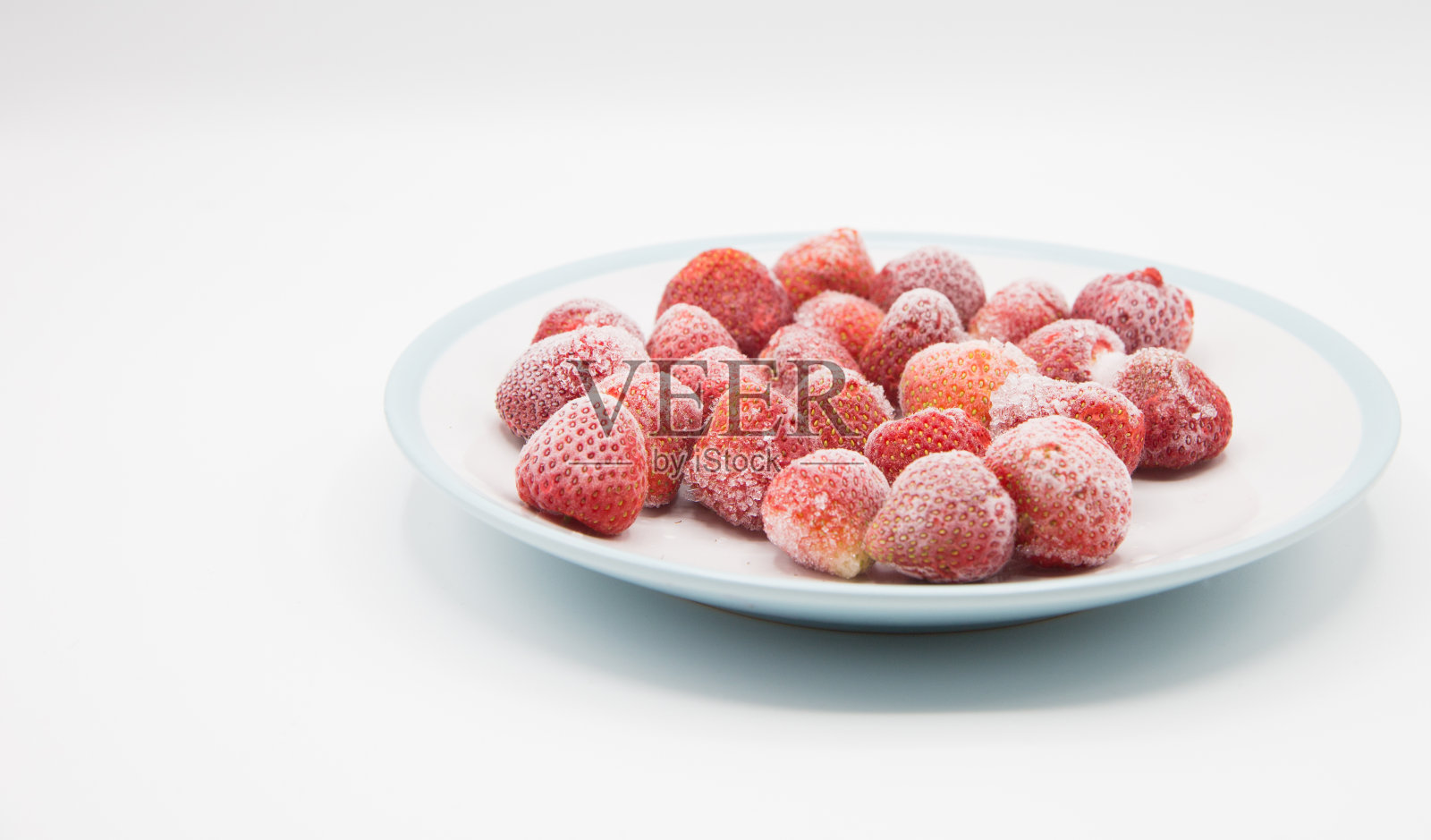 在白色背景前的碗里放着冰冻的草莓照片摄影图片