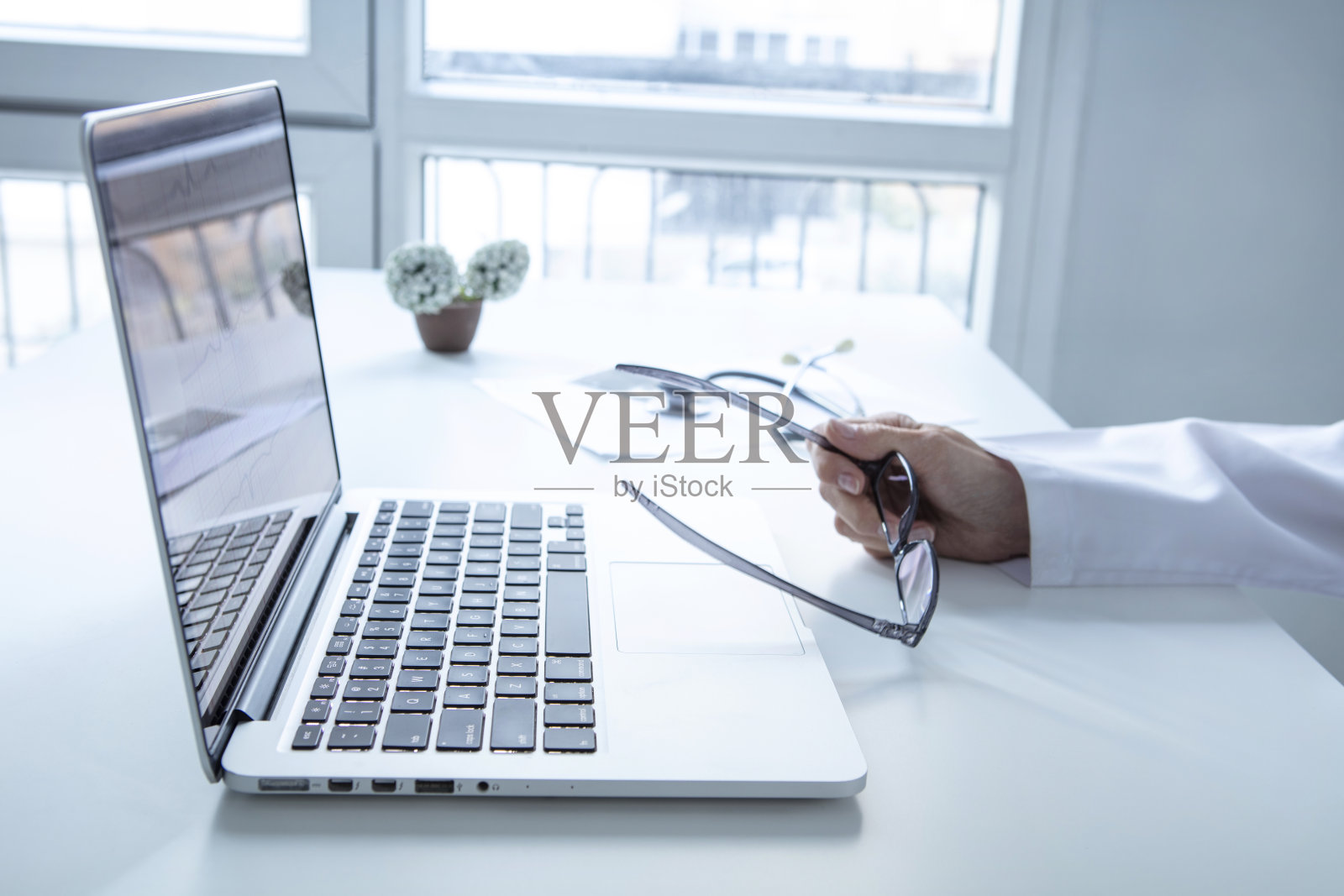 近距离的女医生手拿着一个眼镜在她的工作桌上的笔记本电脑在她的办公室照片摄影图片