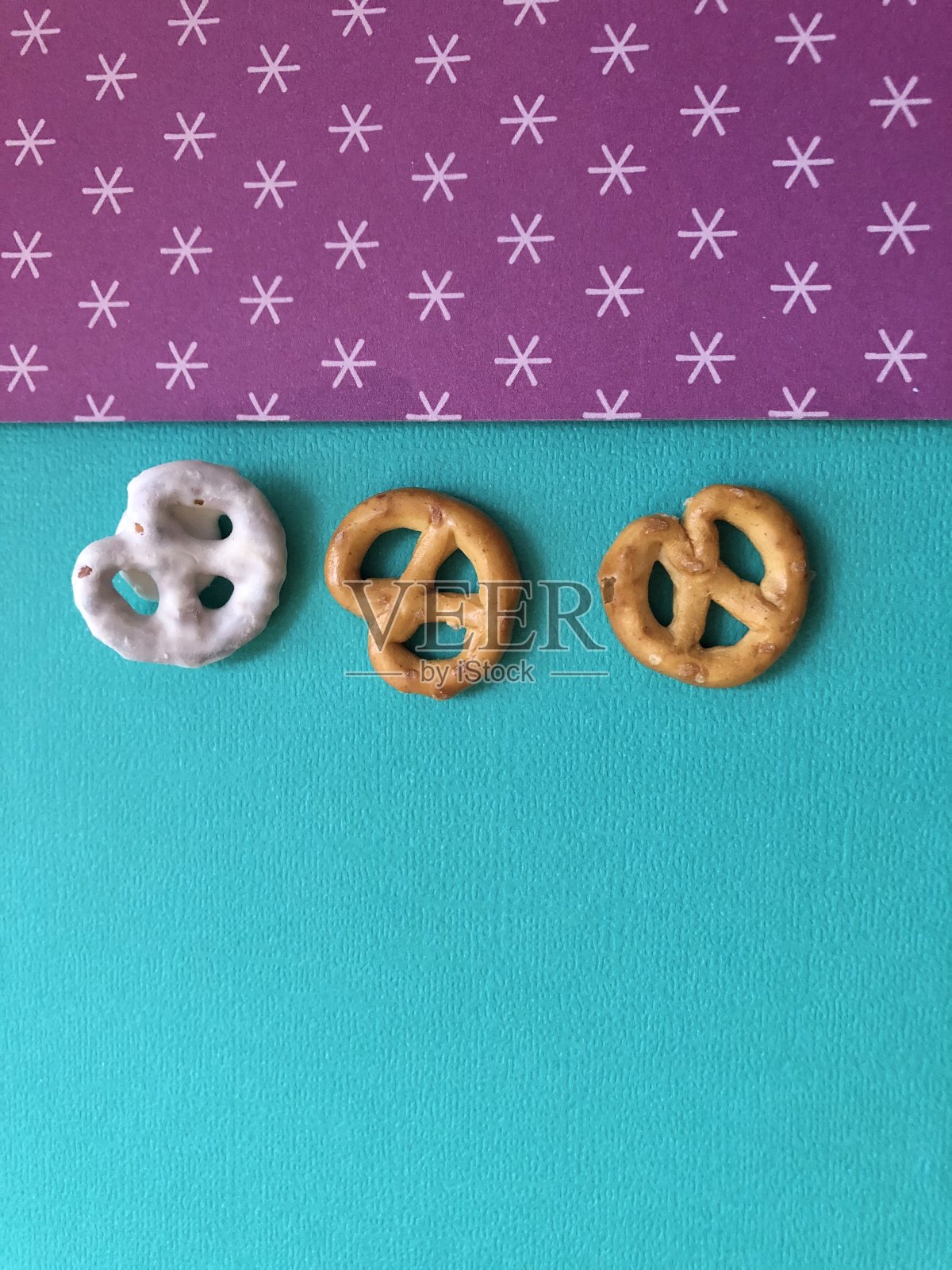 两个椒盐卷饼和一个白巧克力覆盖椒盐卷饼在绿色和紫色图案的背景照片摄影图片