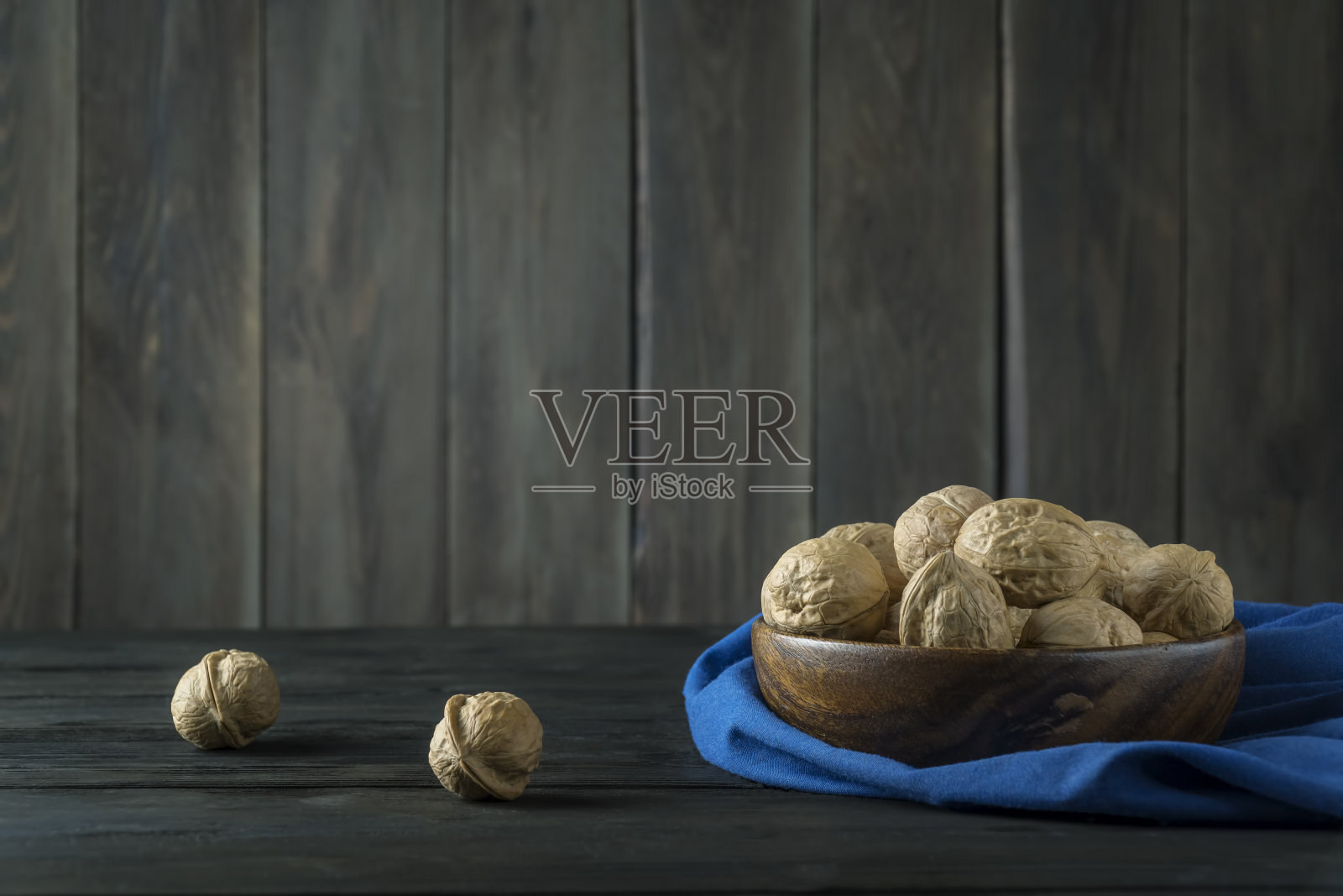 核桃放在一个木碗里，放在一张黑色的木桌上，桌上放着蓝色的餐巾照片摄影图片
