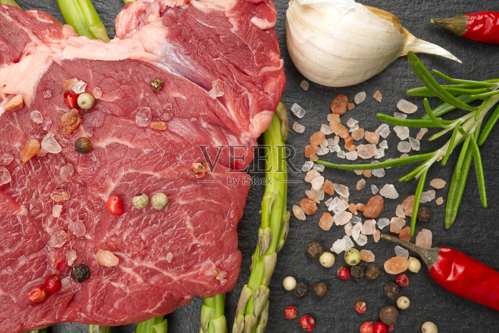 生肋眼牛排配香料和蔬菜。餐厅用餐的配料。鲜肉，盐，迷迭香，百里香，辣椒，圣女果，黑石蒜。食品的背景。照片摄影图片