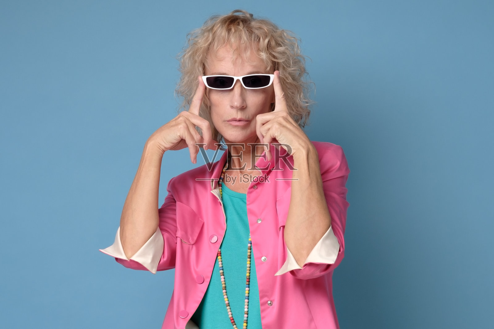 戴着时尚太阳镜、对着蓝色墙壁微笑的老年妇女照片摄影图片