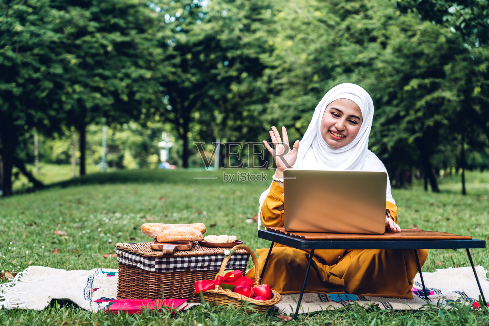 在夏日公园里微笑使用笔记本电脑的快乐阿拉伯穆斯林妇女肖像照片摄影图片