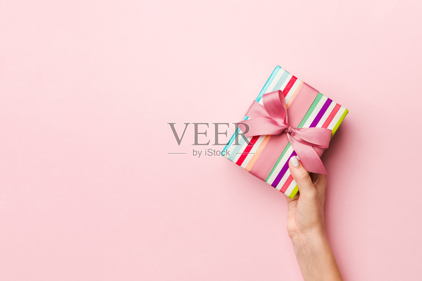 女人的手拿着带彩带的彩条礼盒，以活珊瑚为背景。圣诞概念或其他节日手工礼品盒，概念顶视图与拷贝空间照片摄影图片