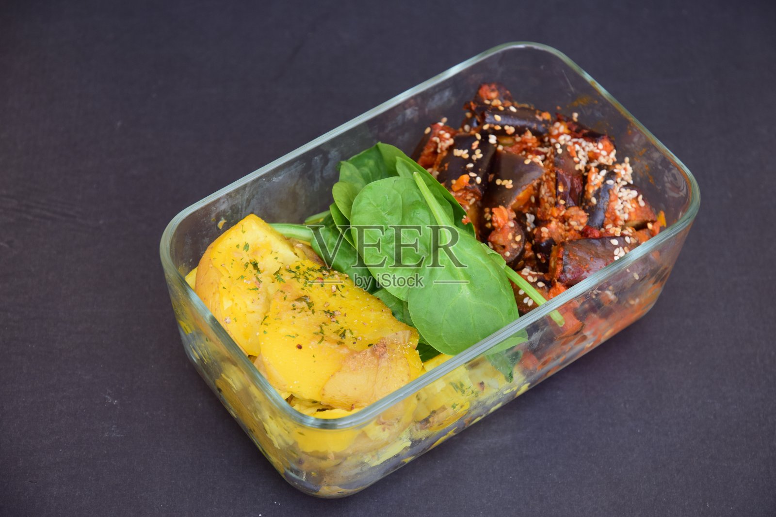 准备家常便饭，用玻璃午餐盒装上哈里萨茄子酱、碎土豆、菠菜和芝麻照片摄影图片