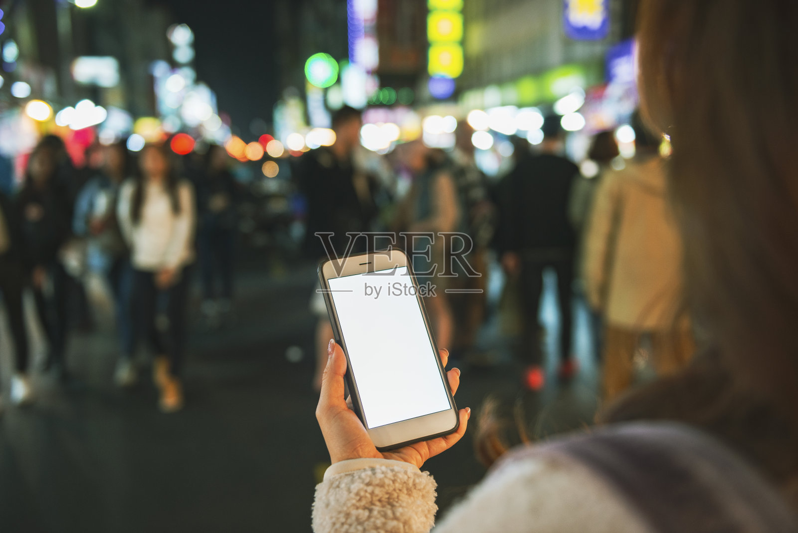 在夜晚，女人用手机对着市中心区发光的霓虹灯商业标志和城市街道照片摄影图片
