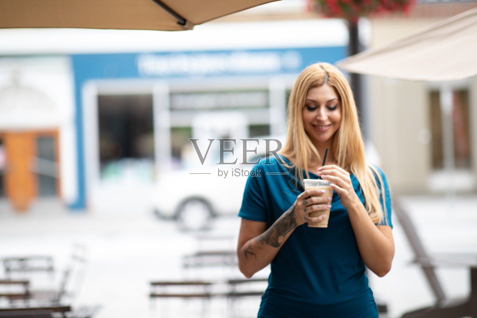 可爱的金发女郎走在一个小城市的街道上，喝着冰咖啡照片摄影图片