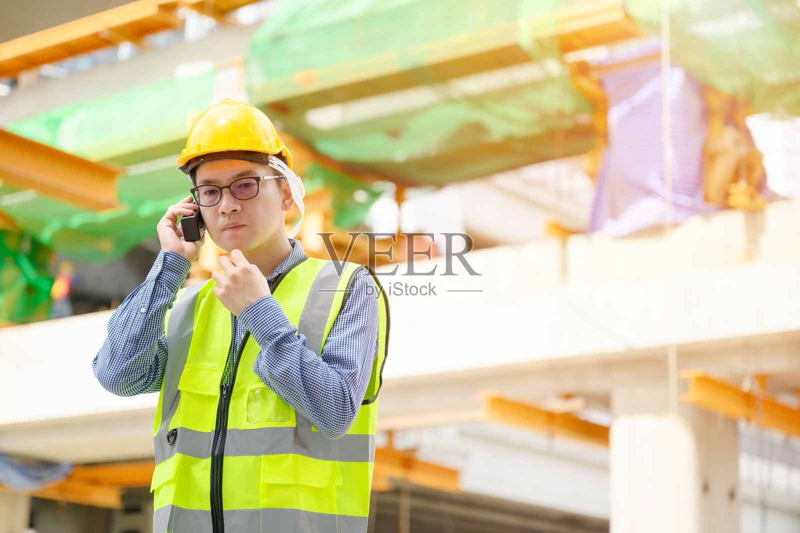 在建筑工地上工作的亚洲工程师，佩戴黄色安全帽和统一工装，手持便携式无线电收发器进行通信照片摄影图片