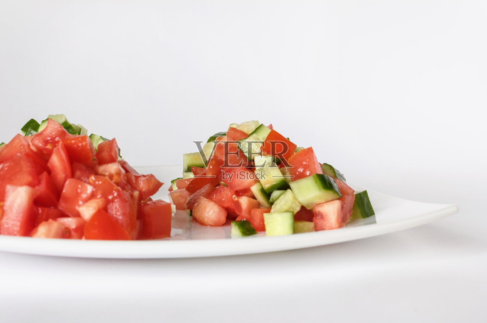 白色盘子里有番茄和黄瓜沙拉。生蔬菜丁。特写镜头。隔离照片摄影图片