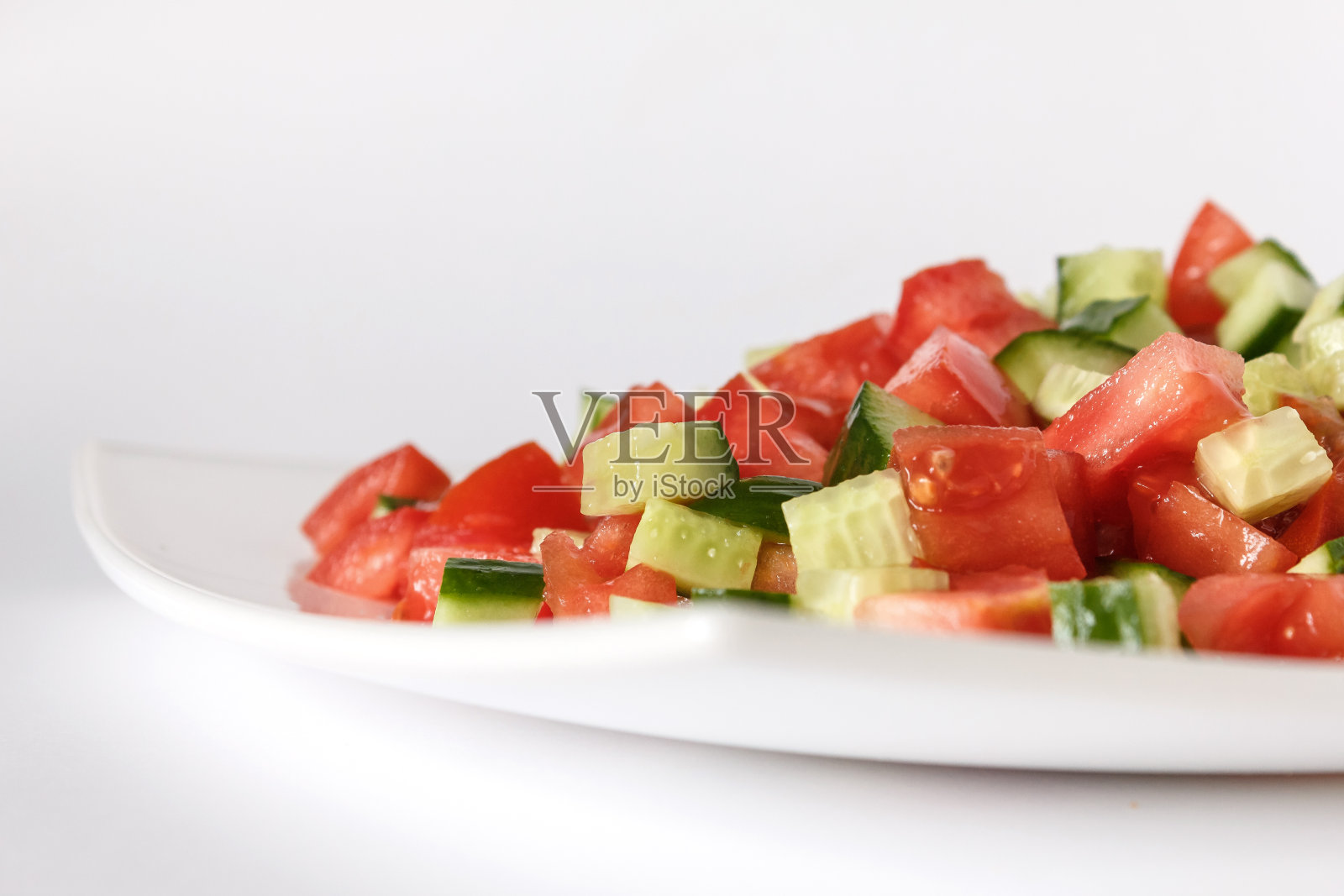 白色盘子里有番茄和黄瓜沙拉。生蔬菜丁。特写镜头。隔离照片摄影图片