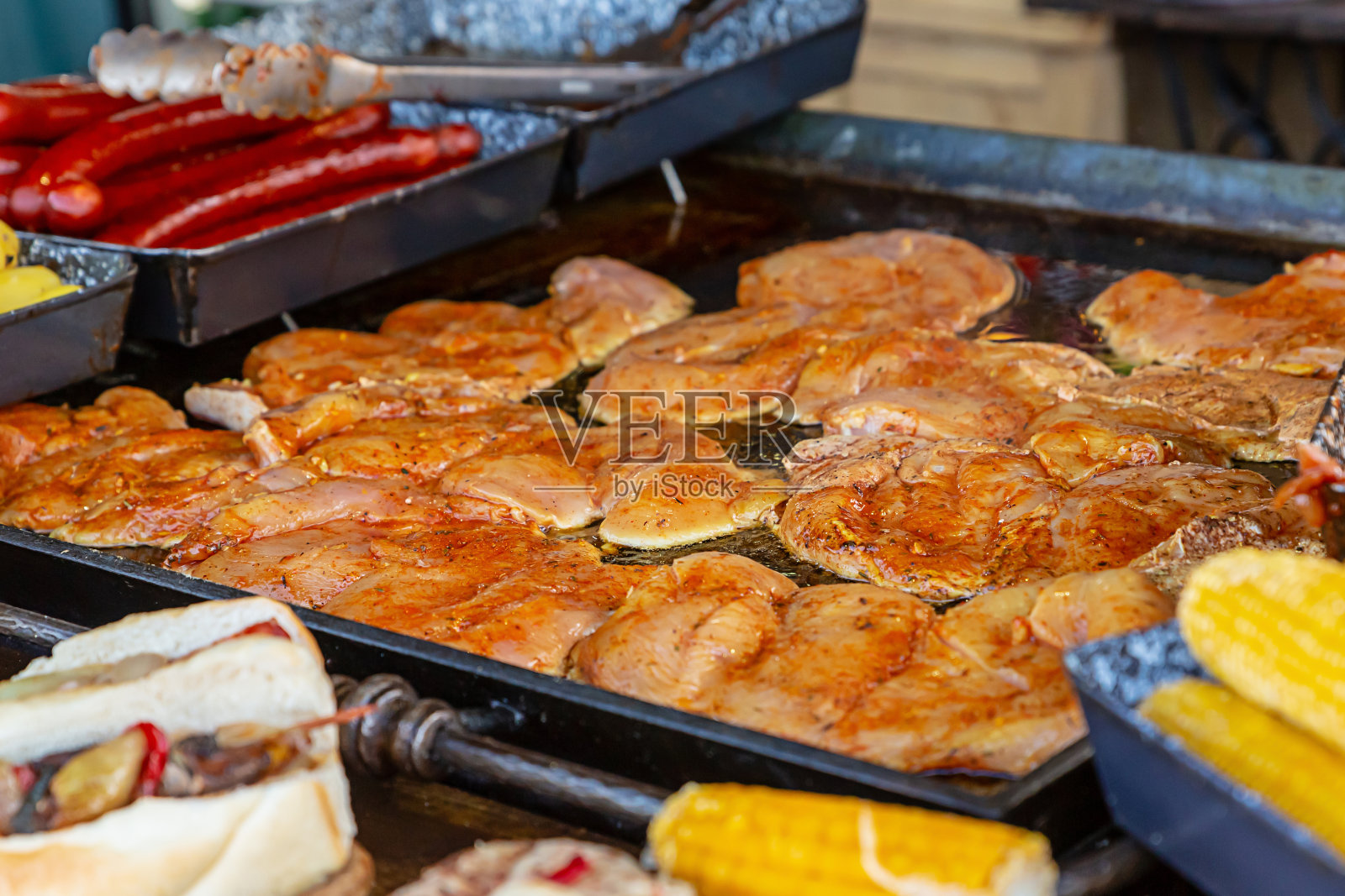 在一个铁盘上，在香肠和玉米中间放着生的调味鸡排，有选择的重点照片摄影图片