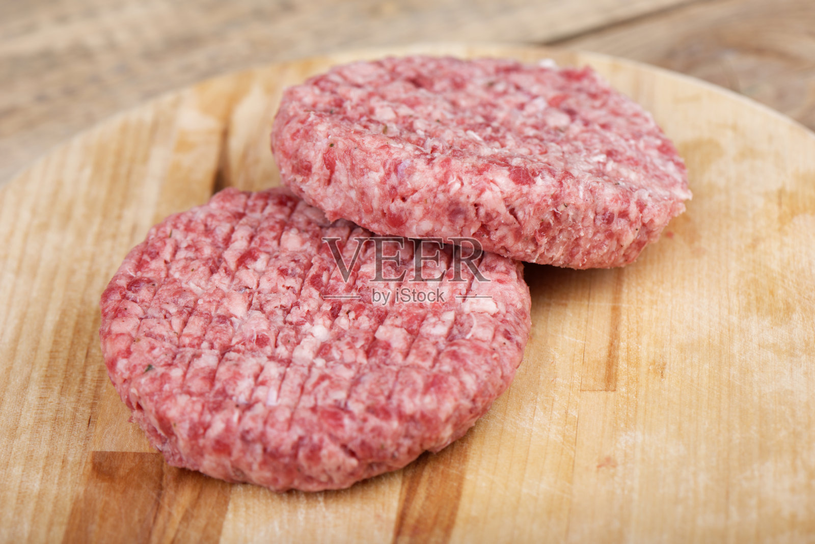 软的焦点。两块生的粉色牛肉片放在砧板上。照片摄影图片