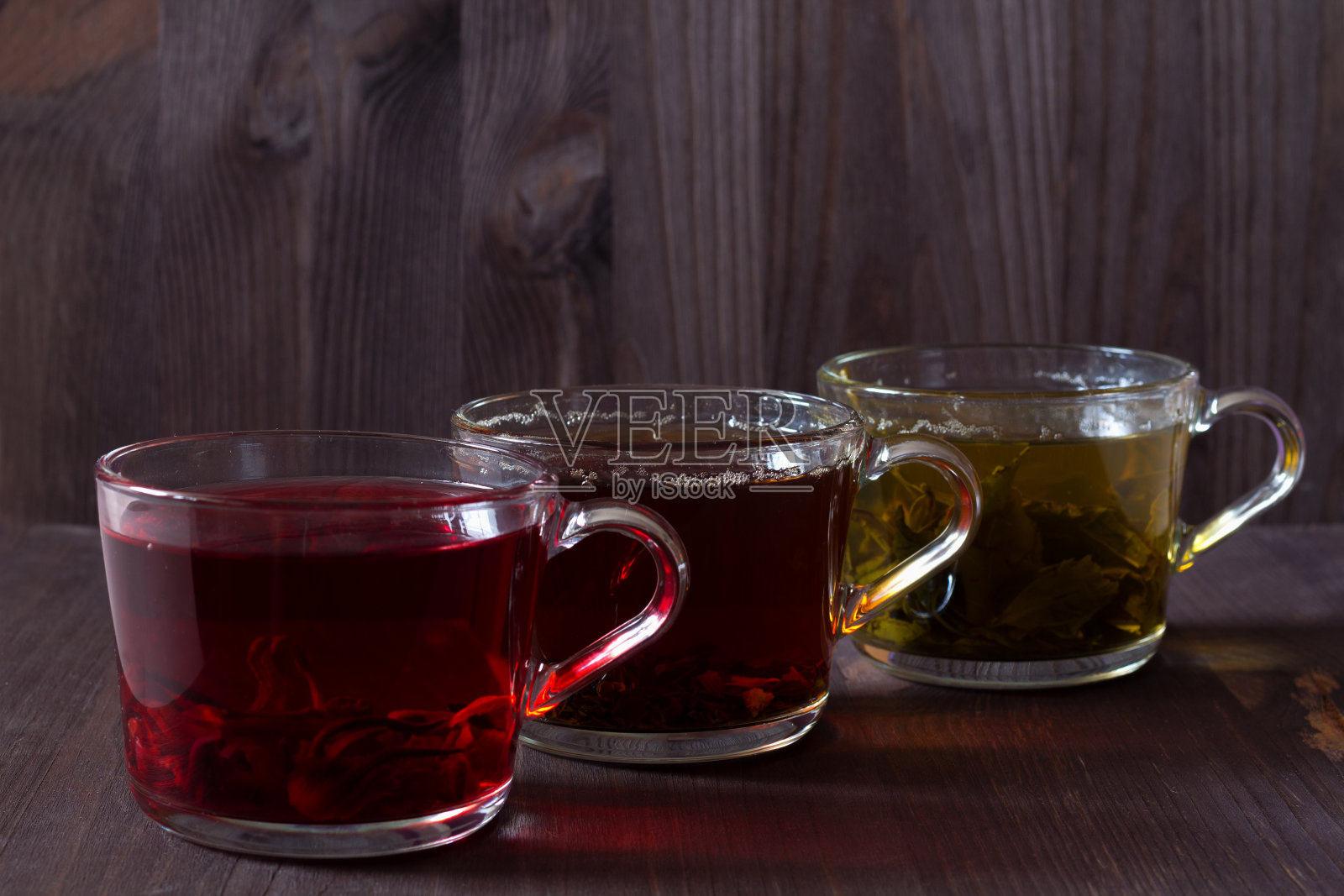 三个杯子，黑色，红色和绿色的茶在一个深色的木制背景。红热芙蓉茶。黑色的热茶。健康的生活方式。热饮料。绿色的热茶放在木桌上。照片摄影图片
