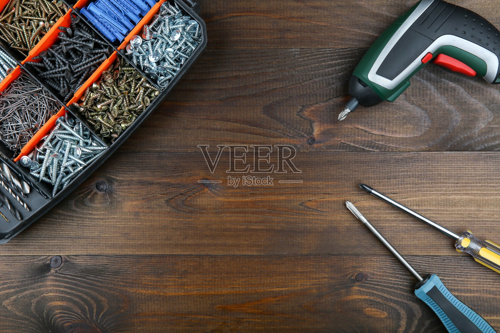 无绳螺丝刀，手动螺丝刀和带有自攻螺钉的盒子，放置在深色木质表面上，中间有拷贝空间，俯视图。照片摄影图片