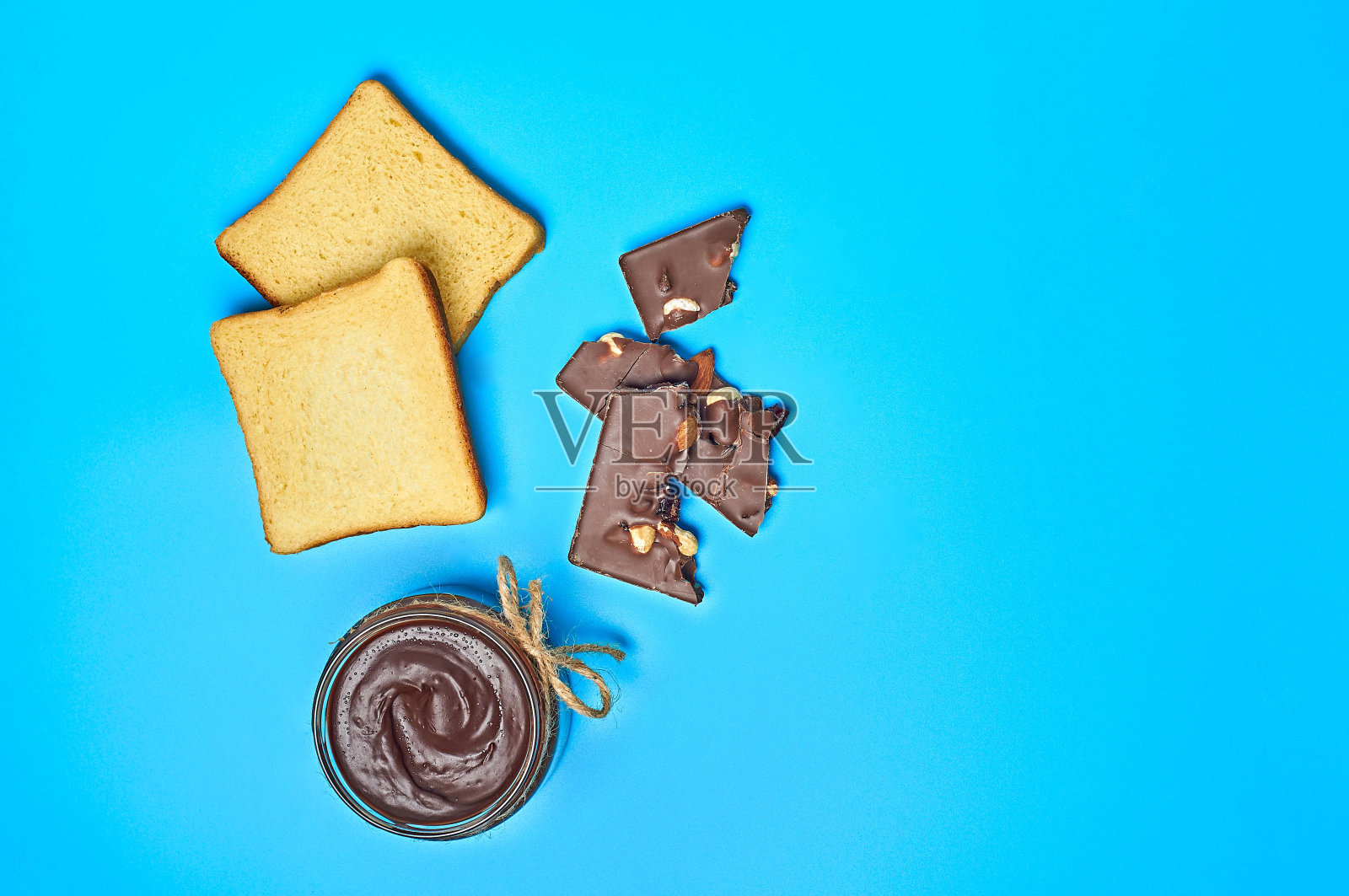 厨房蓝色的桌子上放着一个透明的玻璃罐子，里面装满了融化的巧克力或奶油，旁边放着两片香草面包。营养早餐或午餐的概念照片摄影图片