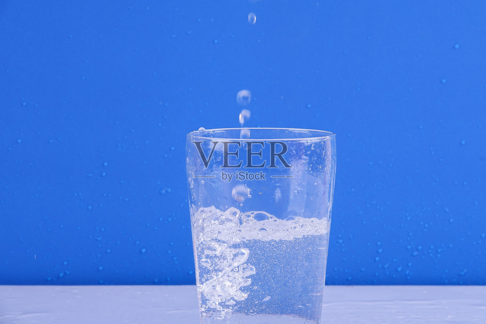 在蓝色背景上，水从孤立的玻璃上溅起。照片摄影图片