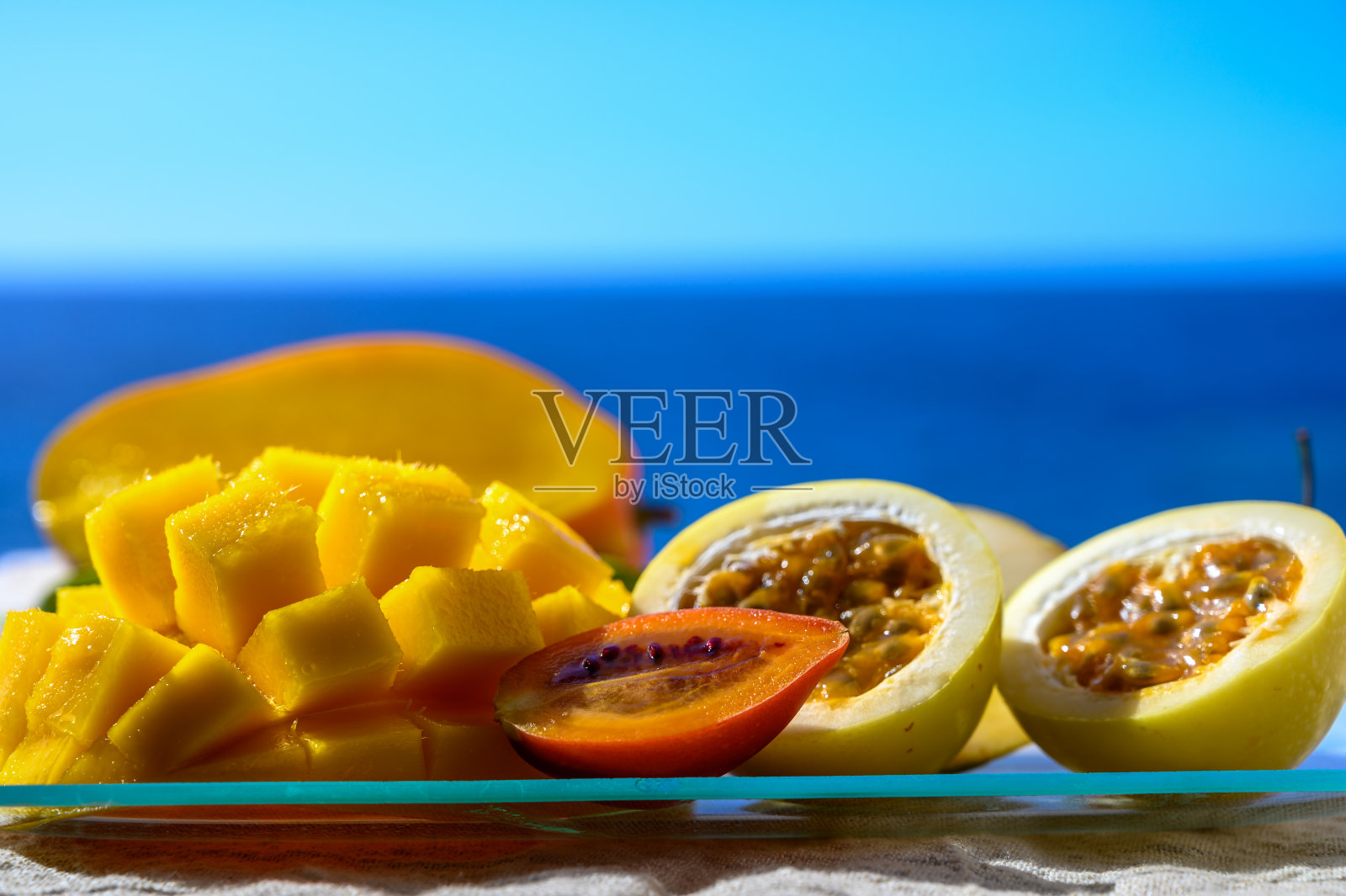 在蓝色的海景背景下，玻璃盘子盛着异国情调的水果，新鲜成熟的甜芒果和百香果照片摄影图片