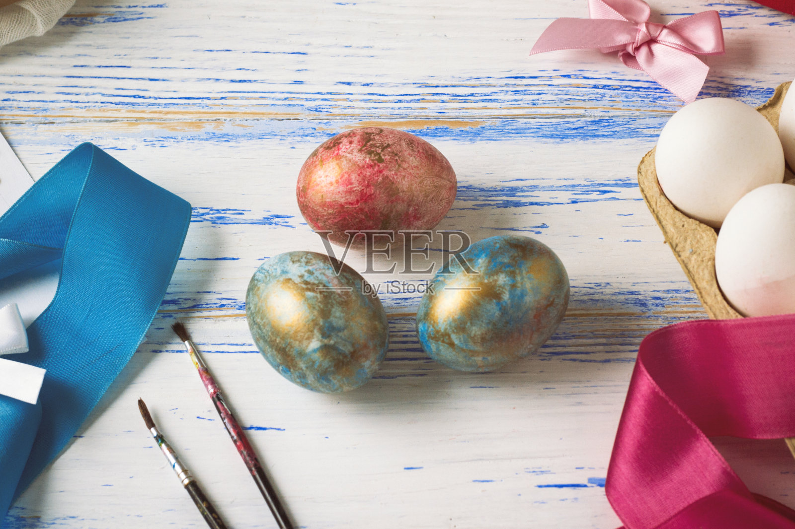 复活节彩蛋和宴会前的彩蛋着色过程。磁带，鸡蛋，刷子，礼物在白色的木制桌子上照片摄影图片