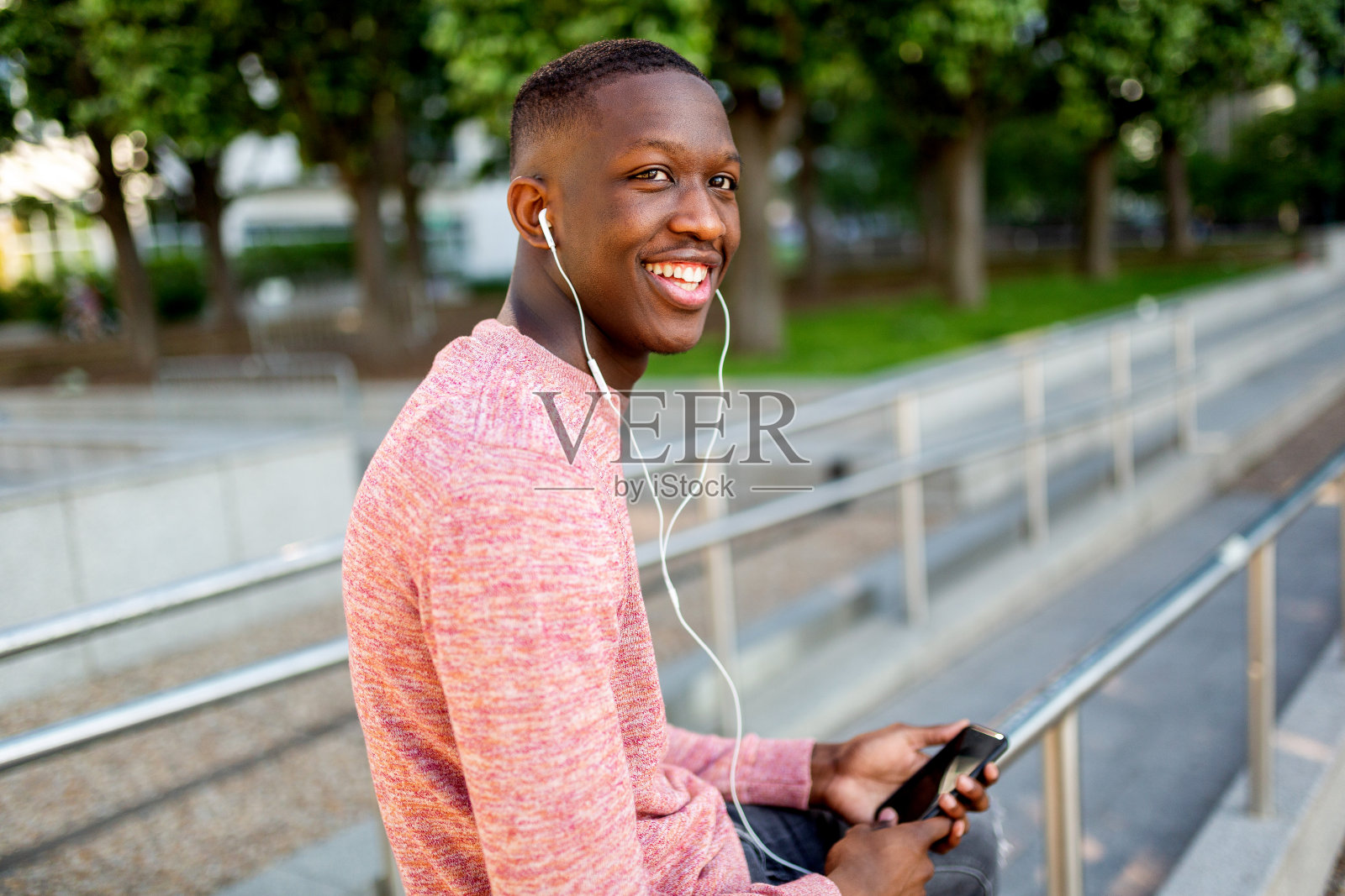 微笑的非洲裔美国青年，戴着耳机用手机听音乐照片摄影图片