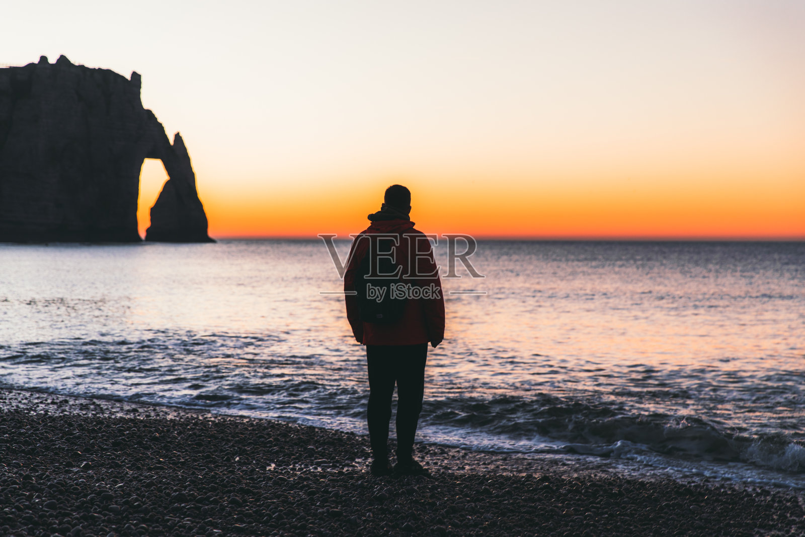 在法国埃特尔塔，一个人欣赏着美丽多彩的日落，在海滩上散步，欣赏着自然拱门照片摄影图片