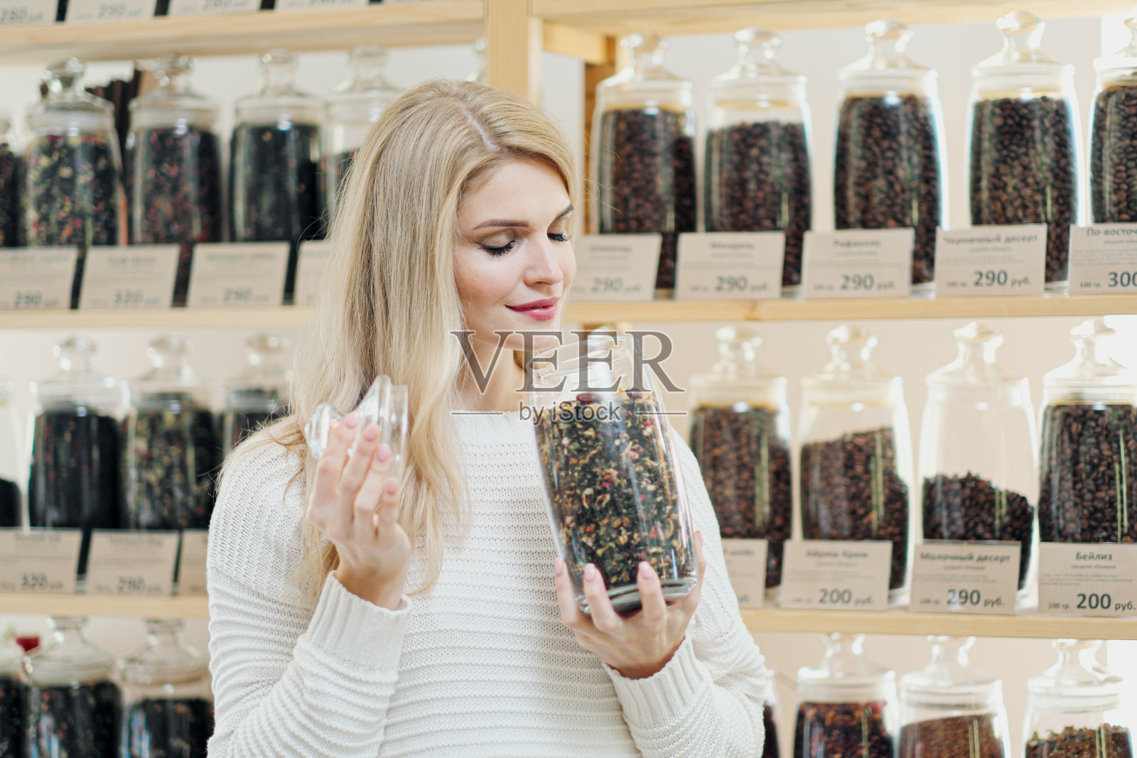 一个年轻的金发女人在商店里挑选麦片咖啡。用一个罐子来测试不同种类的咖啡。照片摄影图片