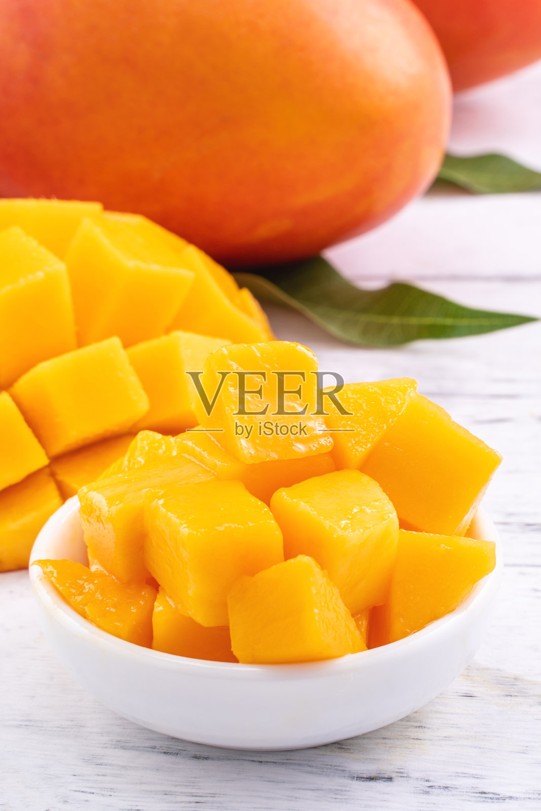 新鲜的芒果，美丽的切好的水果和绿色的叶子在明亮的木桌的背景。热带水果设计理念，拉近距离，复制空间。照片摄影图片