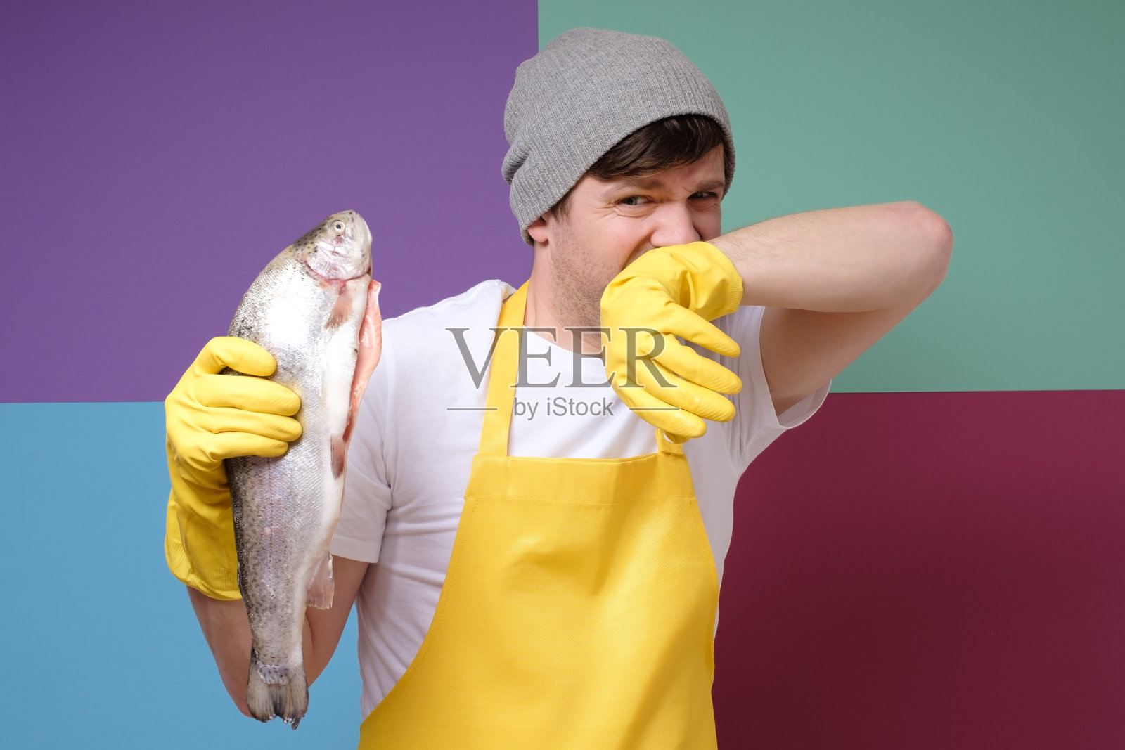 年轻的白人渔民拿着一条腐烂的鱼孤立在彩色背景照片摄影图片