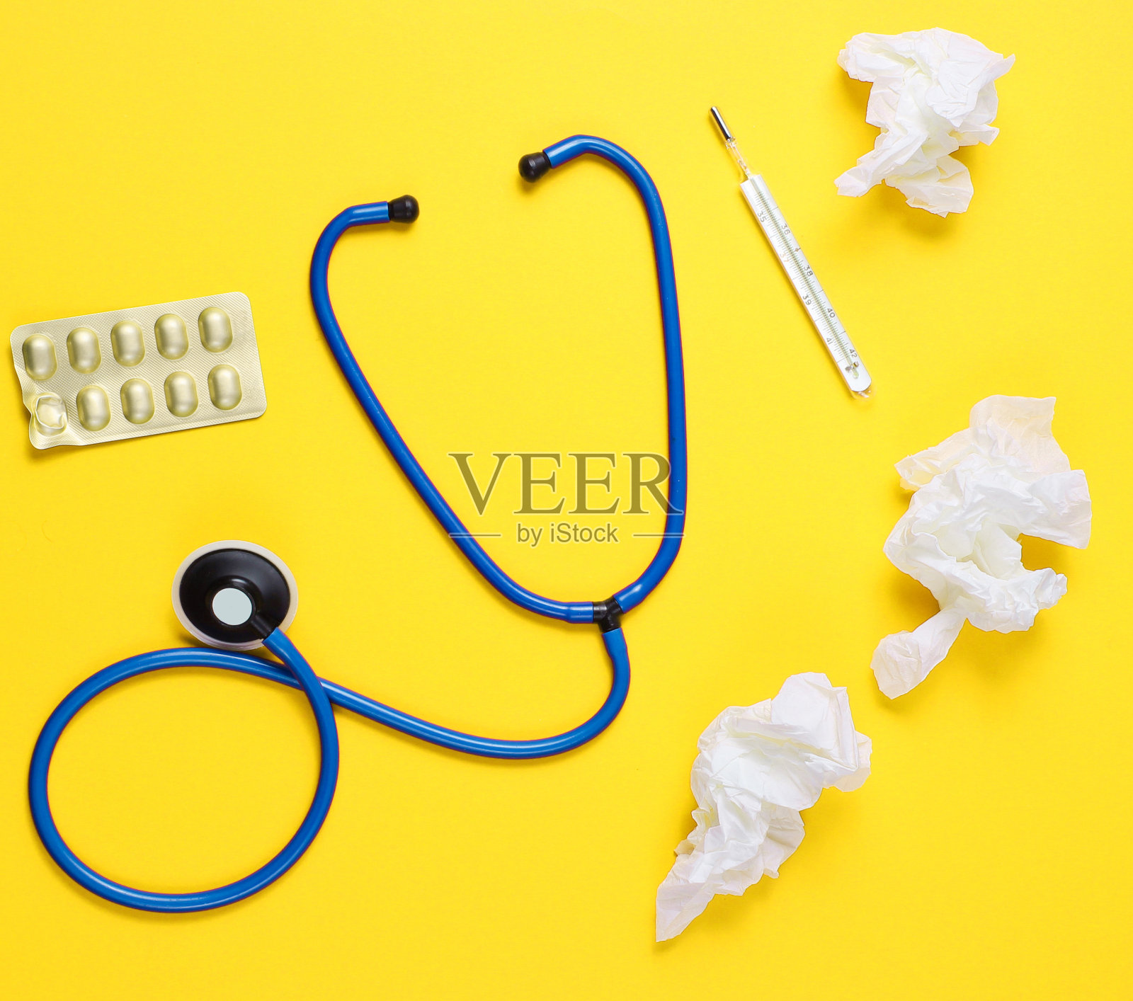 治疗感冒的概念。用过的擦鼻巾、体温计、药片、听诊器在黄色背景上。俯视图照片摄影图片