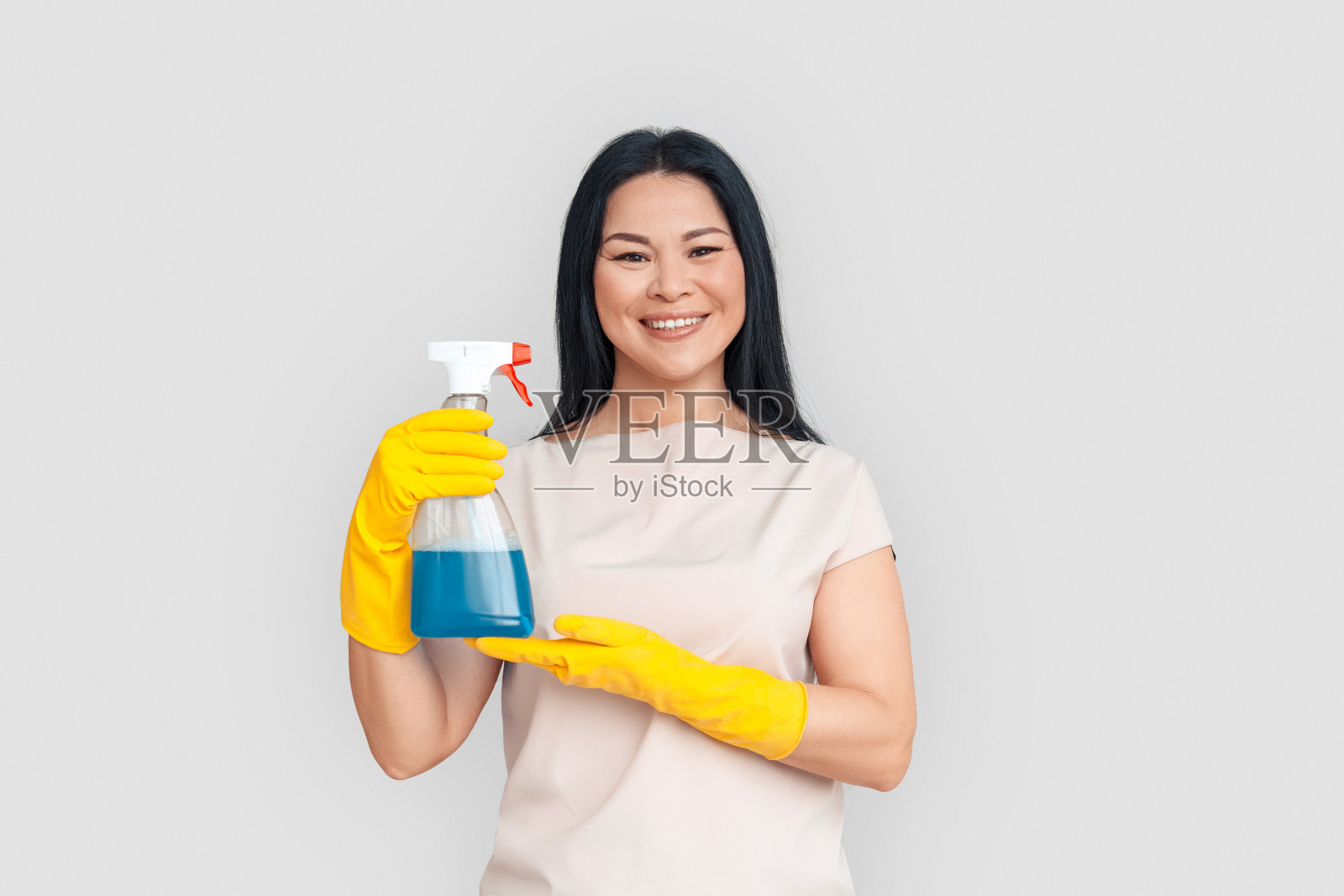 自由式。戴手套的亚洲女人在白色背景下，拿着喷雾开朗地笑着照片摄影图片