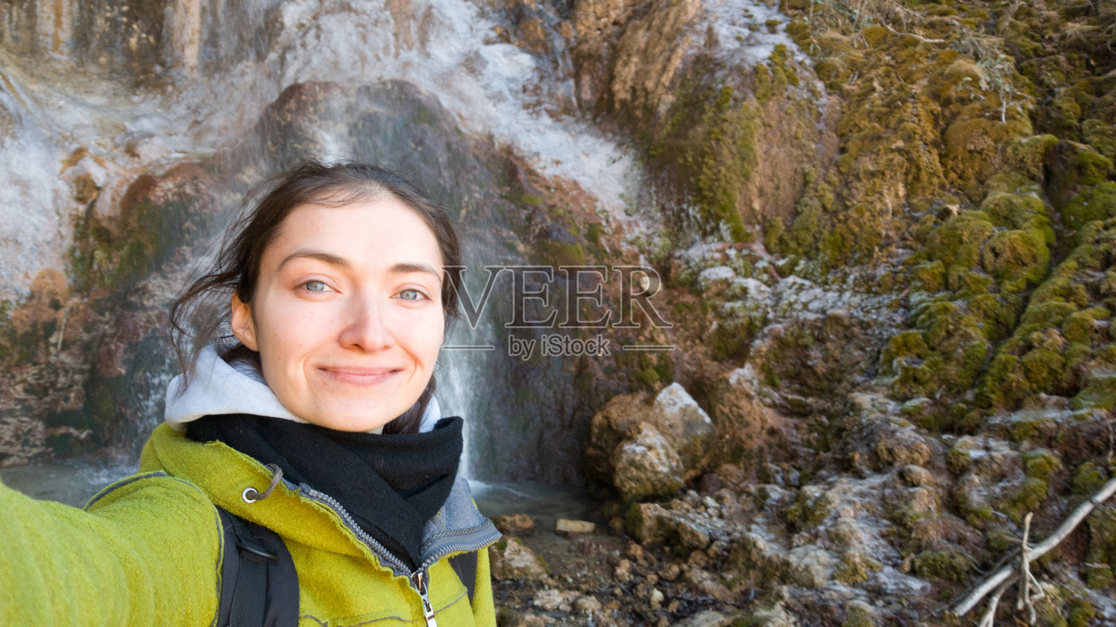 深棕色头发女孩在山和瀑布的背景下自拍，秋冬季旅行，微笑的人们，快乐的旅行照片摄影图片