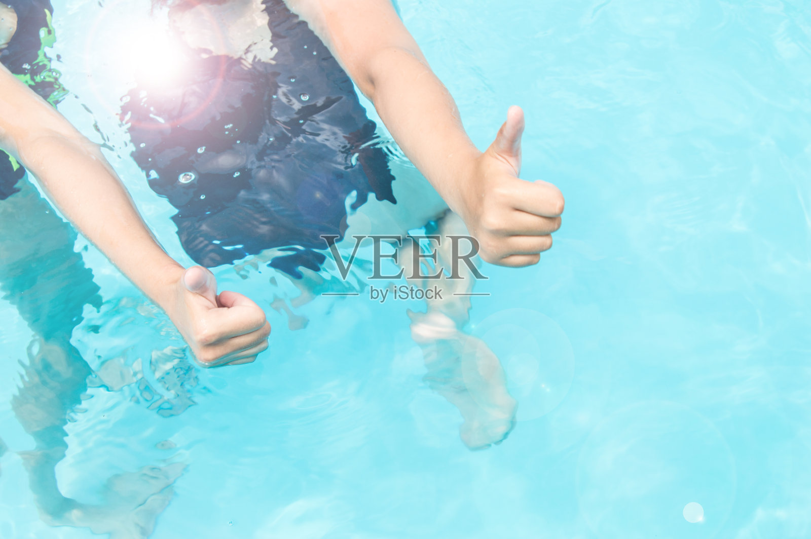 在阳光明媚的夏日里，两个穿着泳衣的长发少女在游泳池里竖起大拇指，蓝色的水闪闪发光照片摄影图片