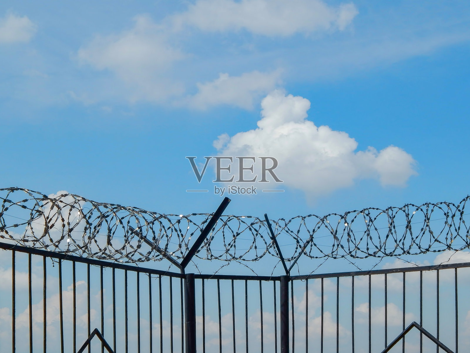 用铁丝网缠绕的铁栅栏映衬着蓝天和有纹理的云彩照片摄影图片
