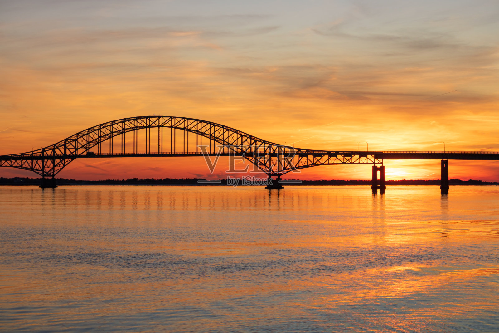 横跨海湾的钢系拱桥在夕阳下的水中倒影清澈。照片摄影图片