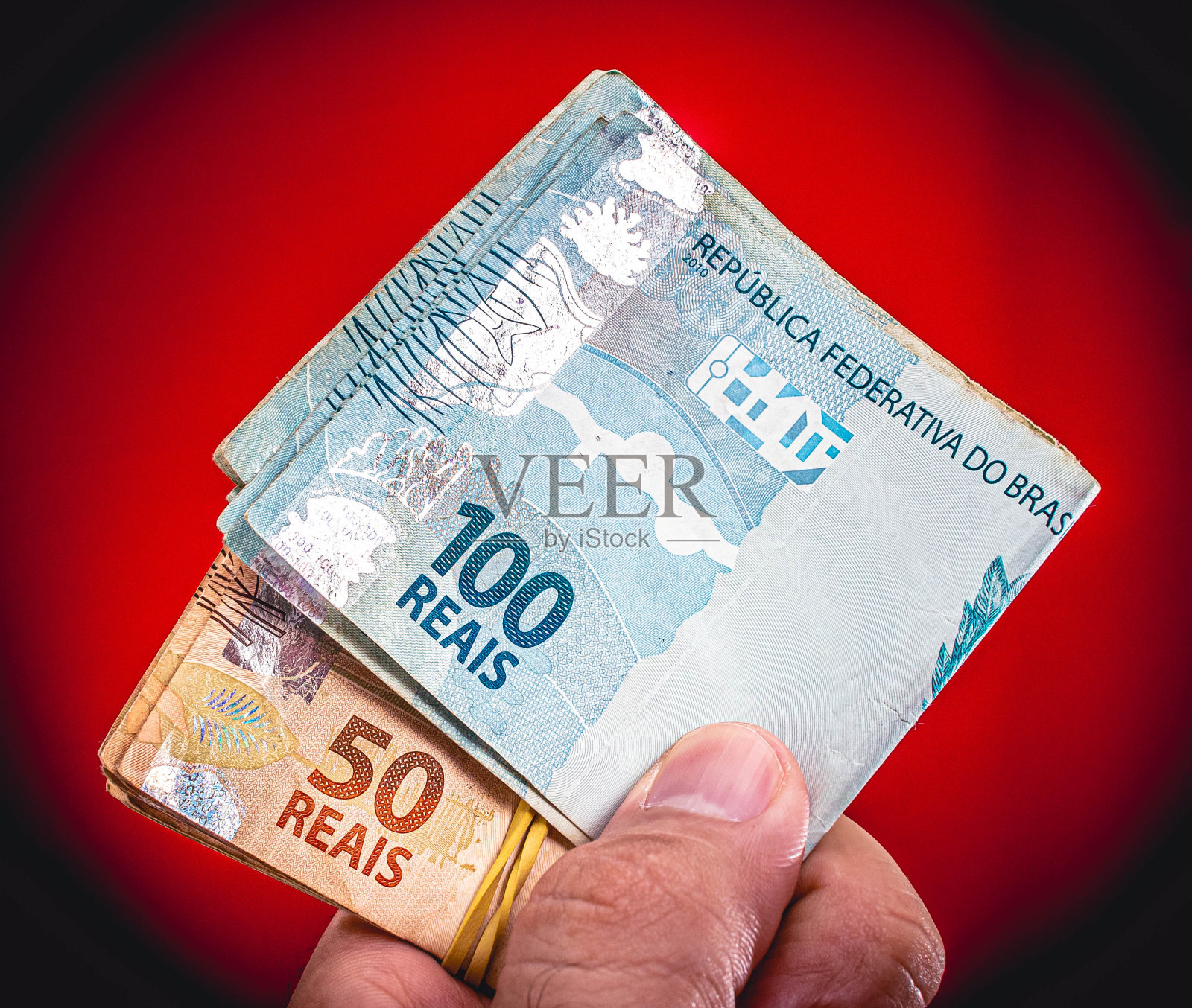 巴西货币：巴西雷亚尔。手持巴西货币的男人（摄影棚红色背景）照片摄影图片