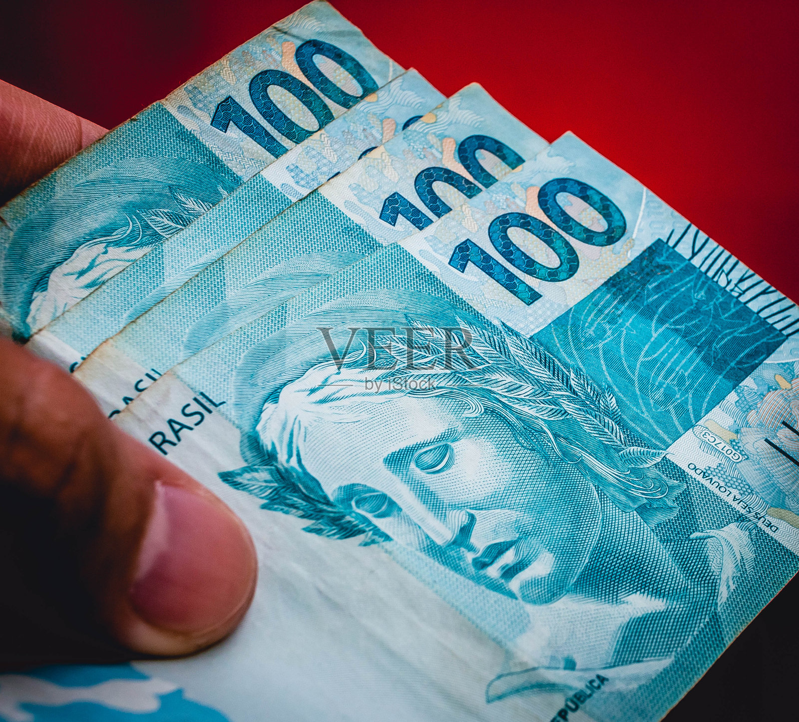 巴西货币：巴西雷亚尔。手持巴西货币的男人（摄影棚红色背景）照片摄影图片
