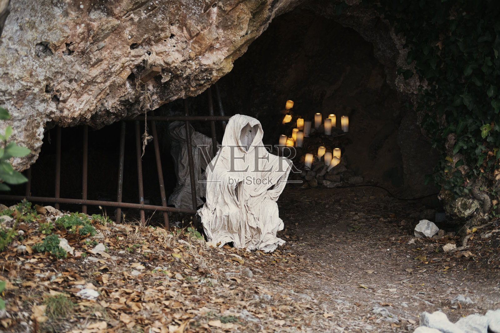 白色斗篷带兜帽的鬼在洞口点着蜡烛。神秘的形象照片摄影图片