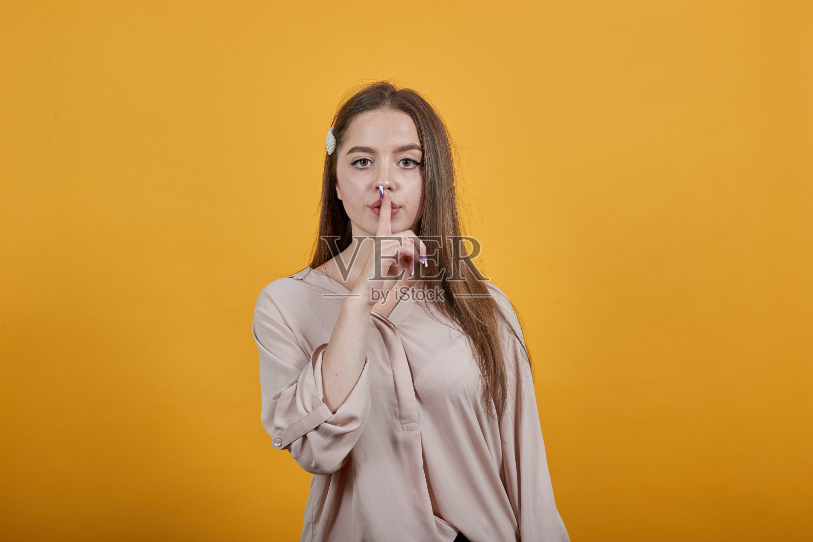 淡色衬衫的冷静女人手指一直放在嘴上，沉默，做嘘的手势照片摄影图片