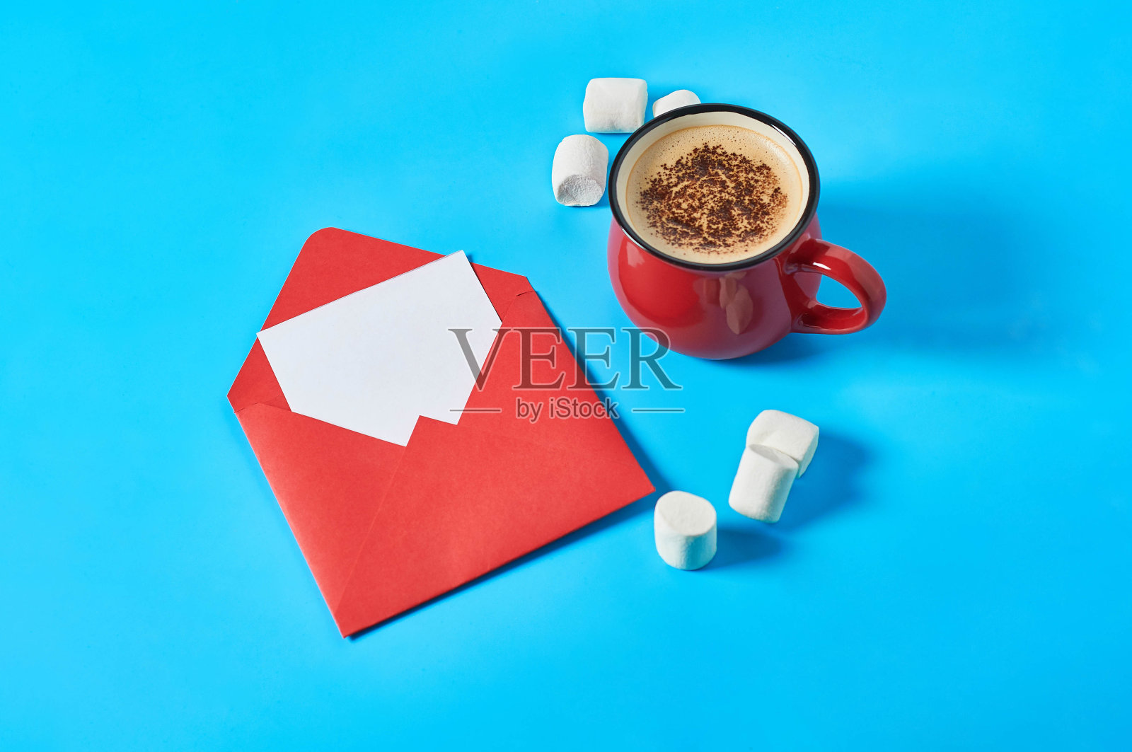 蓝色的桌子上放着一张空纸和满满一杯咖啡，信封旁边散落着棉花糖。情书的概念。特写镜头照片摄影图片