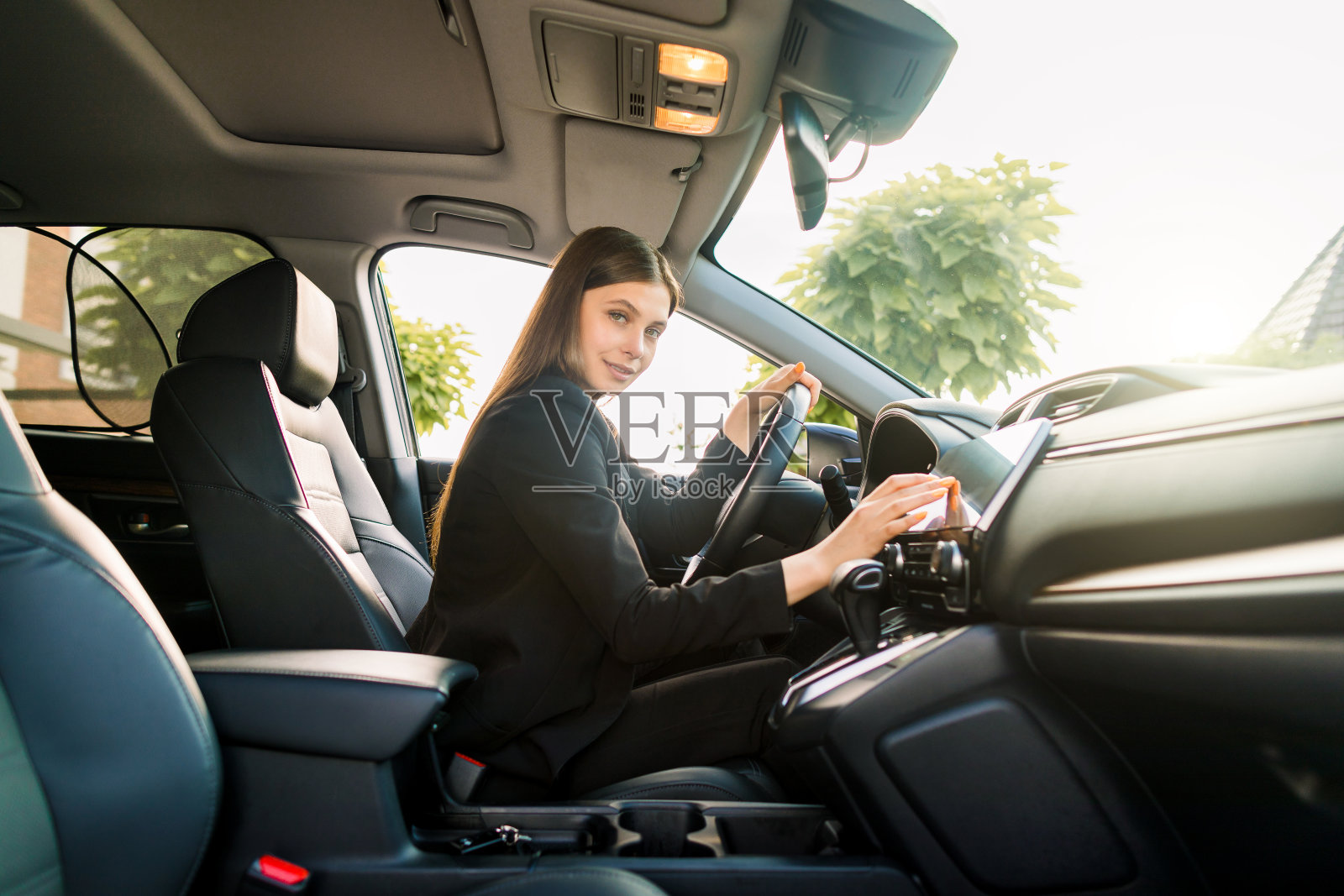 美丽微笑的年轻女子黑色西装驾驶汽车，迷人的女孩坐在汽车，户外夏季肖像。照片摄影图片