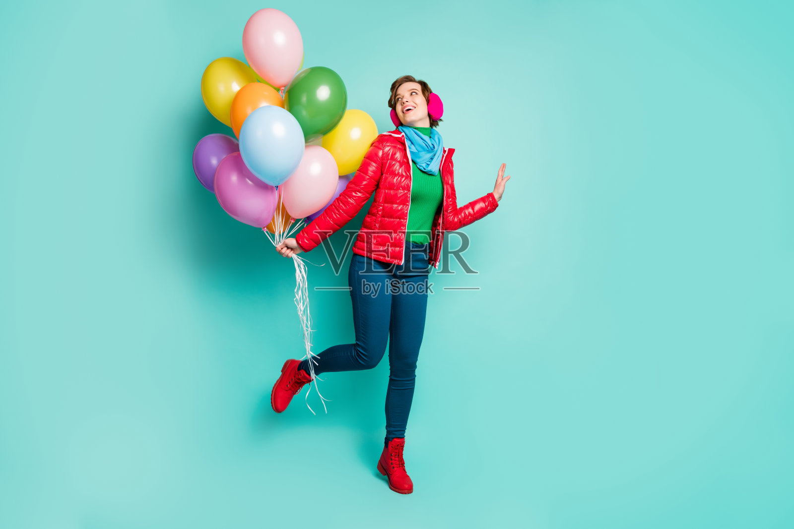 全身照片有趣的不寒而冻的女士来了生日派对带来了许多五颜六色的气球穿休闲的红色外套围巾粉色耳套裤子鞋子孤立的蓝绿色背景照片摄影图片