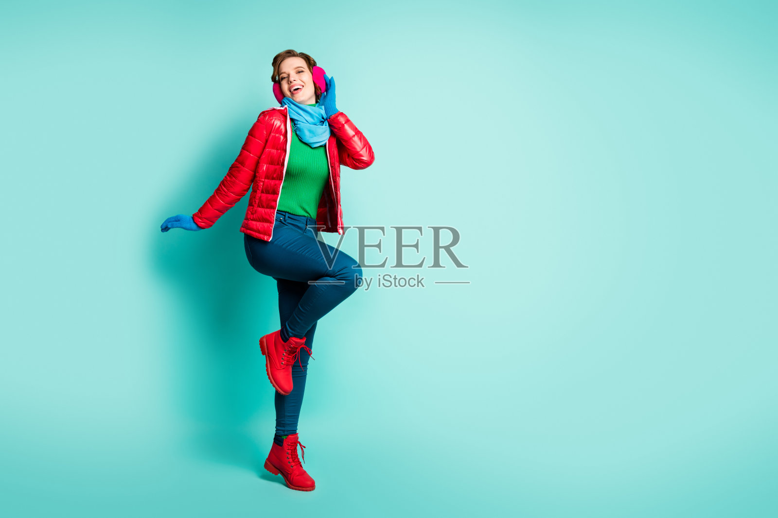 有趣的漂亮的女士享受冬天的一天走在街上度过最好的空闲时间穿休闲的红色大衣围巾粉红色的耳朵保暖裤鞋子孤立的蓝绿色背景照片摄影图片