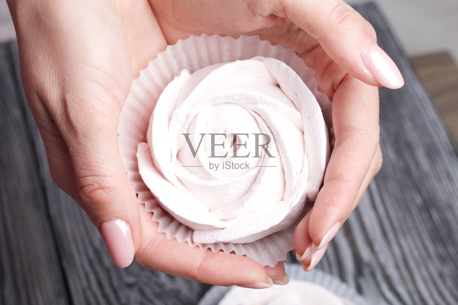 在一个女人的手掌上的玫瑰形状的棉花糖。以刷过的黑色和白色松木板为背景。照片摄影图片