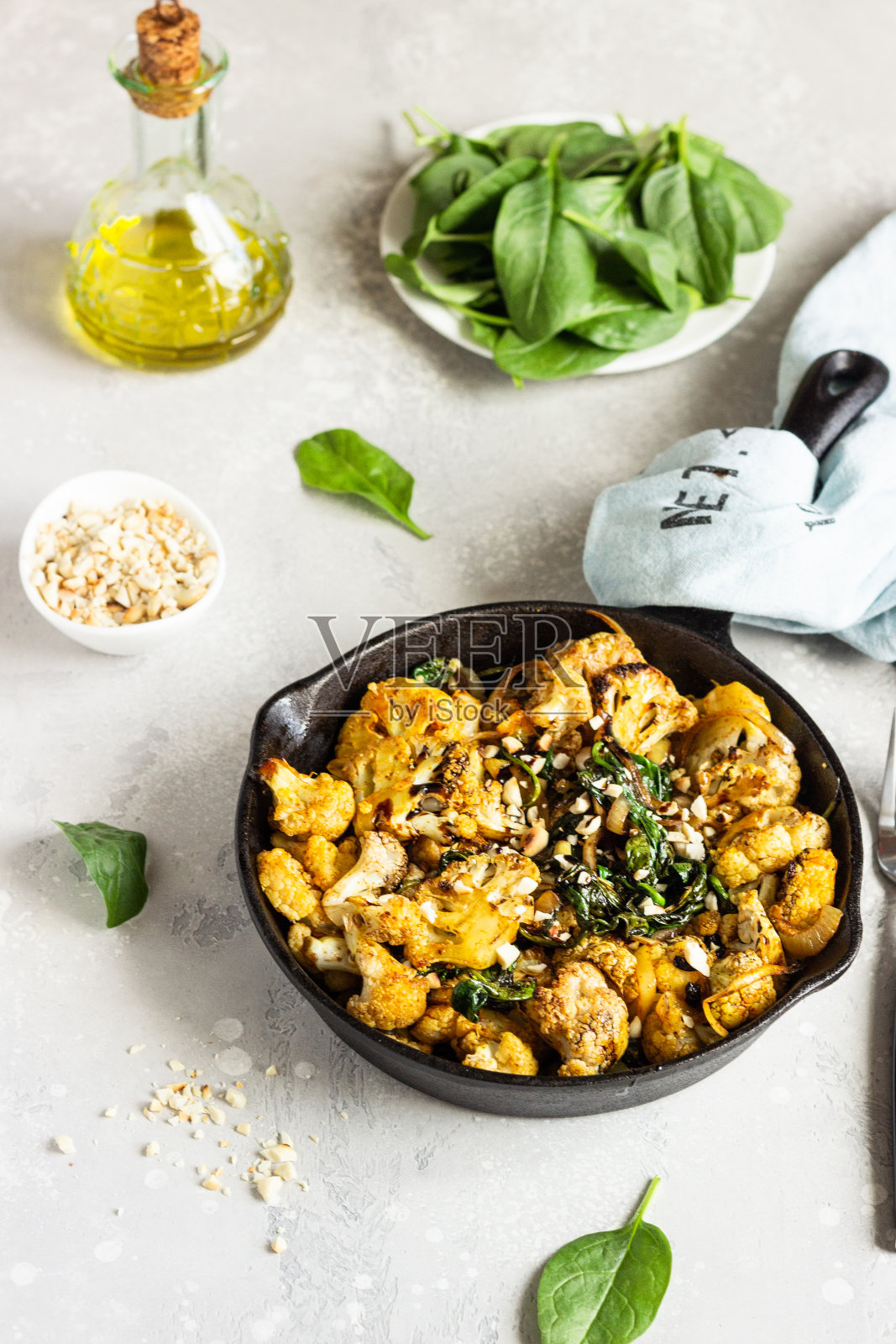 烤花椰菜，菠菜，葡萄干和坚果在铸铁平底锅。浅灰色的背景。副本的空间。健康的素食。照片摄影图片