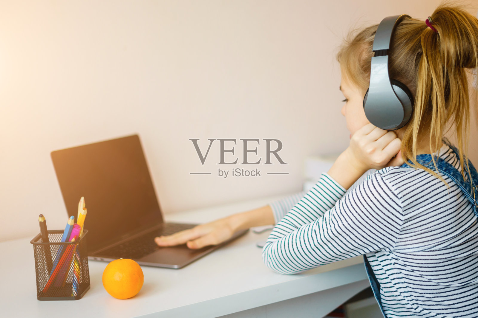 在家中书桌前，戴着耳机用笔记本电脑上网课，并做笔记的少女肖像照片摄影图片