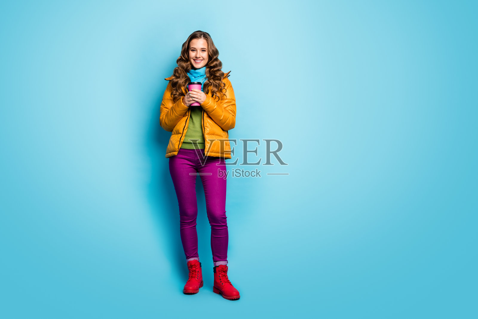 漂亮的女士拿着热的纸饮料杯的全身照片享受温暖的天气穿休闲的黄色大衣围巾紫罗兰色裤子红鞋套头衫孤立的蓝色背景照片摄影图片