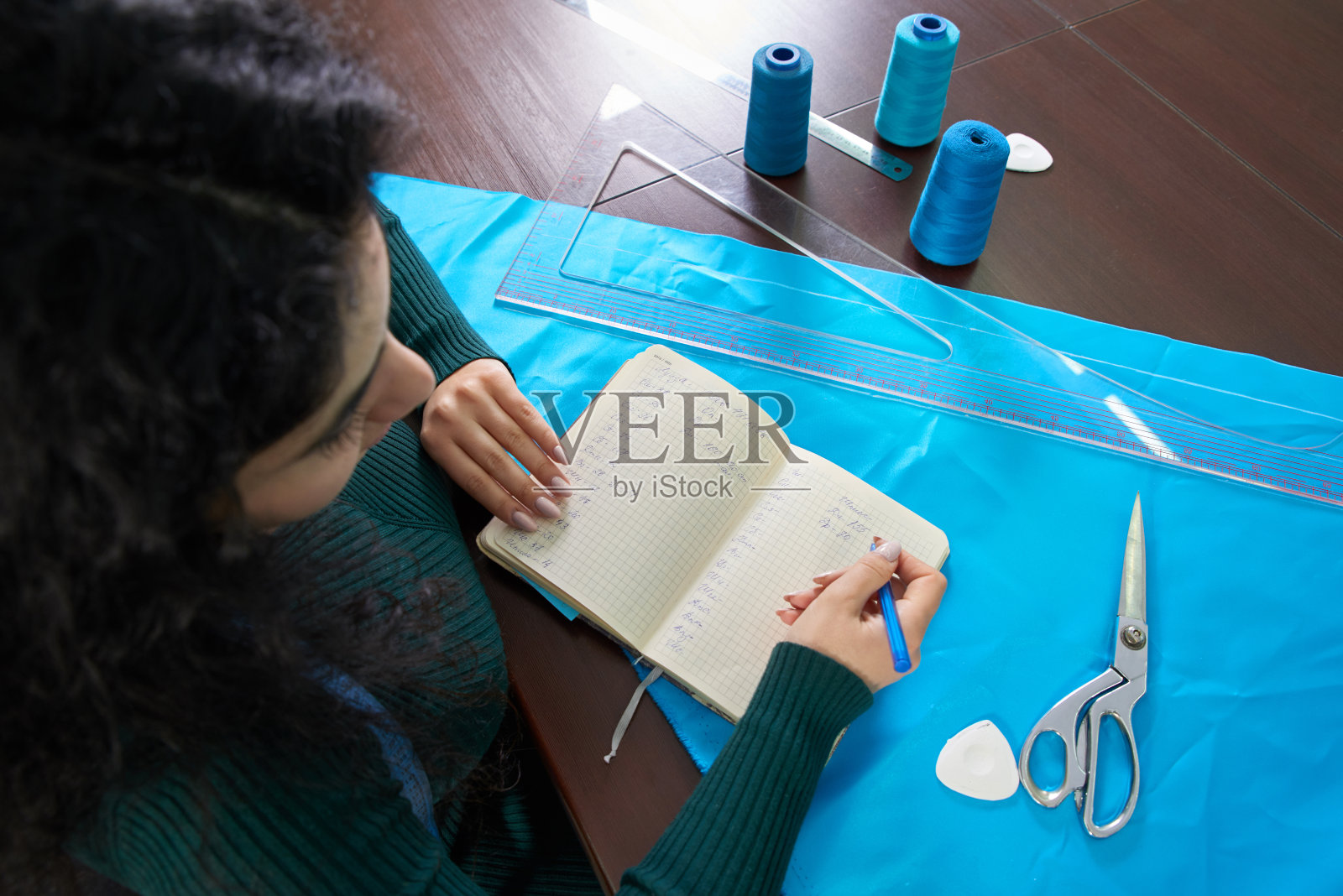 女裁缝把尺码记在笔记本上。裁缝设计了一套服装。年轻的女设计师把想法记在笔记本上照片摄影图片