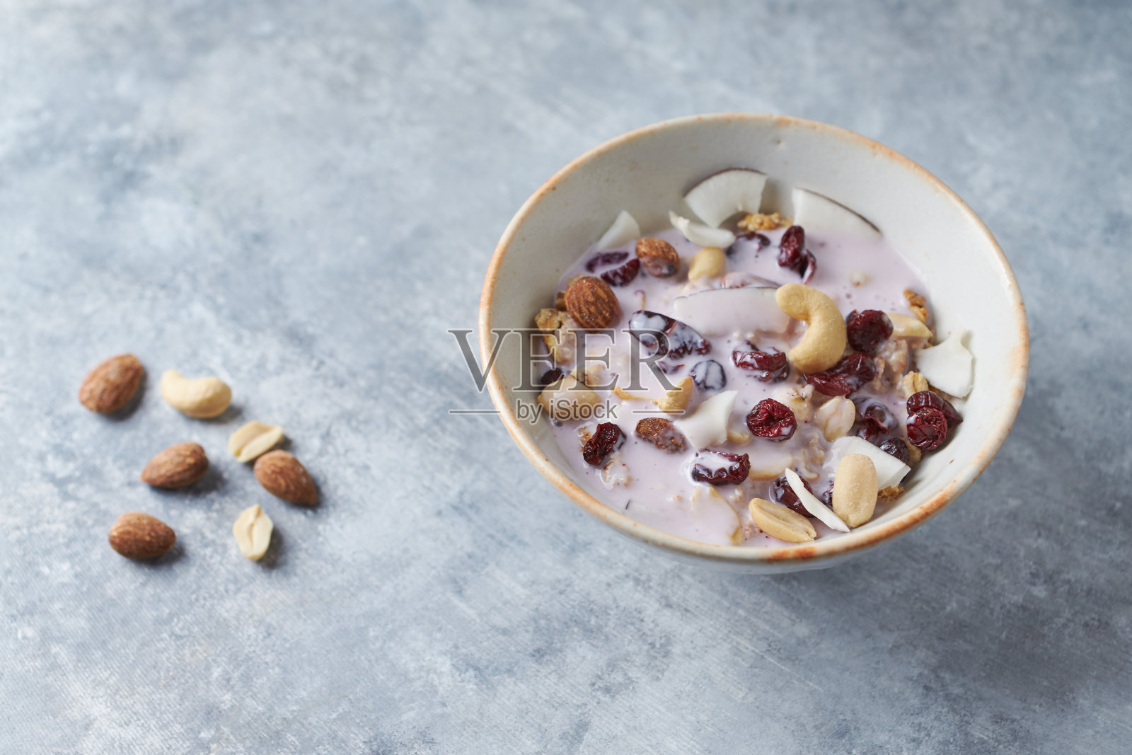 一碗搭配酸奶、坚果、蔓越莓和椰子的格兰诺拉麦片，背景是明亮的石头。照片摄影图片