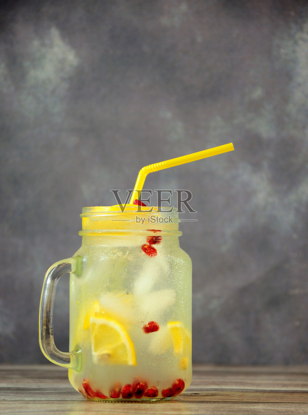 木桌上放着一只玻璃杯，里面放着柠檬水和冰，里面有成熟的石榴籽。照片摄影图片