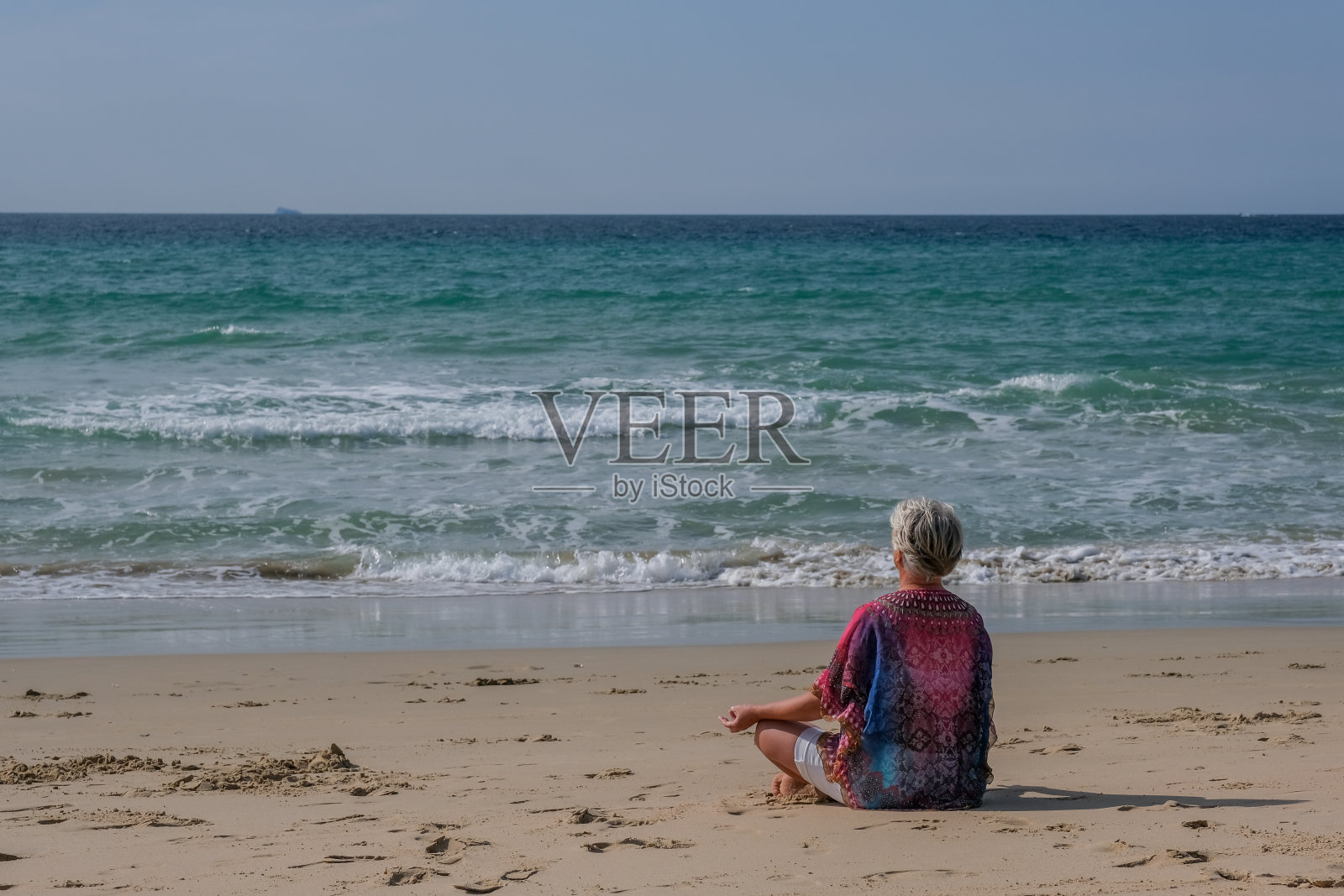 年长的女人与灰色的头发和白色的裙子放松在海滩头发沉思在海滩上照片摄影图片